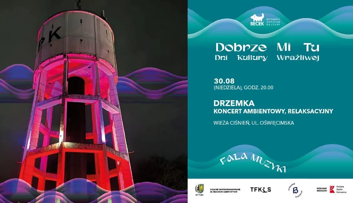 A water tower illuminated with red light and blue-purple wave-like projections, next to a teal poster for a cultural event.